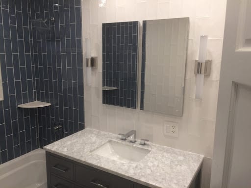 Blue vertical subway tile shower beside marble vanity with wall mirrors