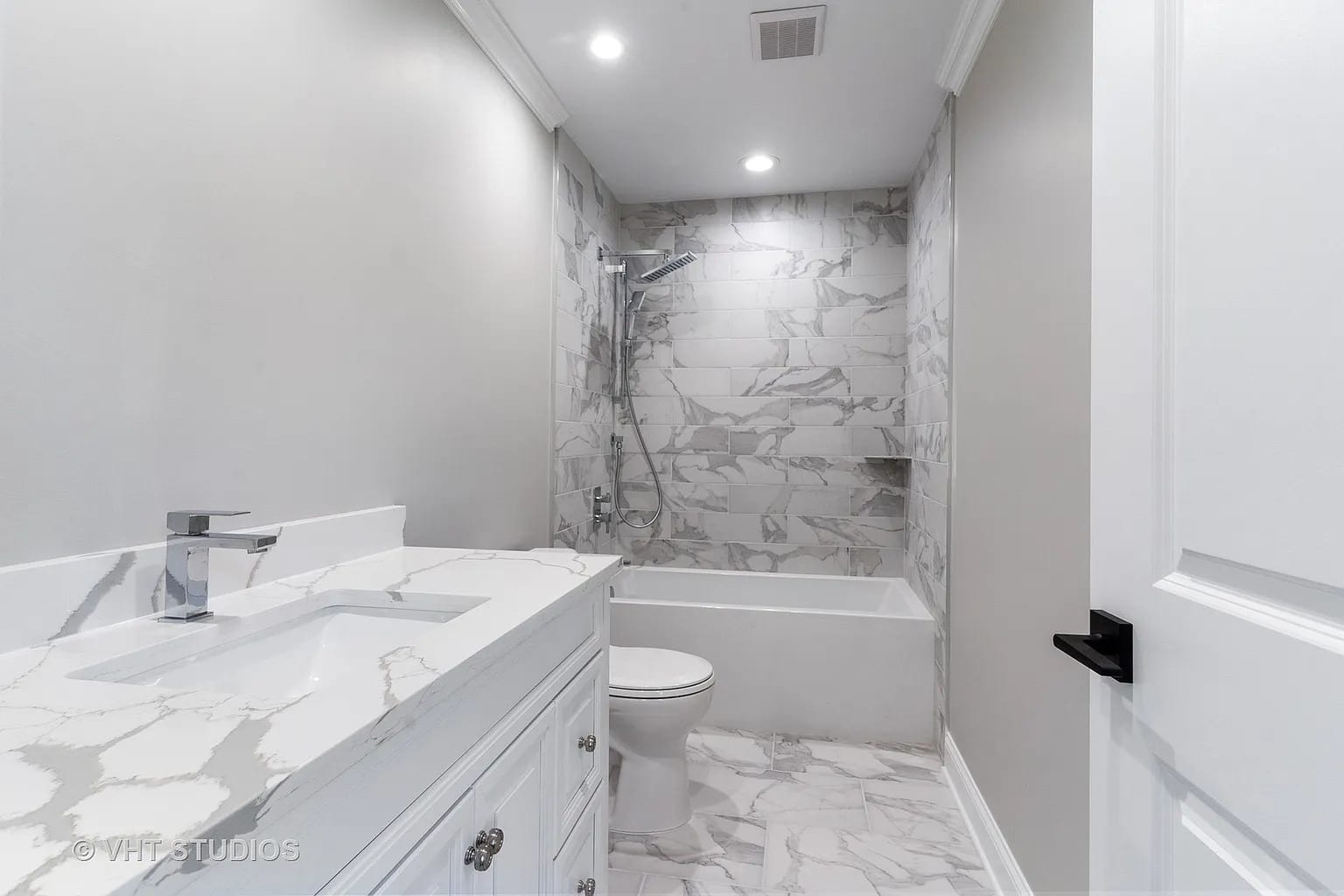 Marble-tiled bathroom with white vanity, soaking tub, and chrome shower fixtures